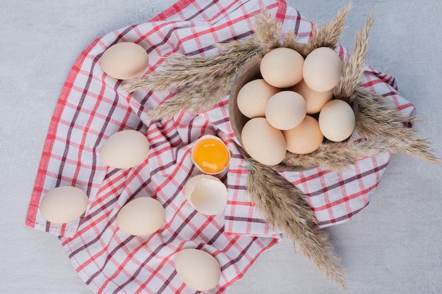 Eggs and feather grass stalks in and next to a bowl on a towel on marble table.