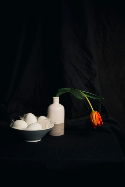 Eggs and feathers near faded orange flower in vase