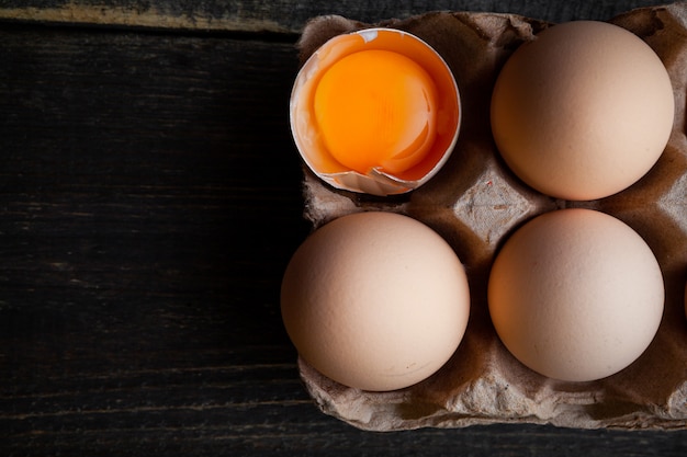 Eggs with broken one top view on a dark wooden background space for text