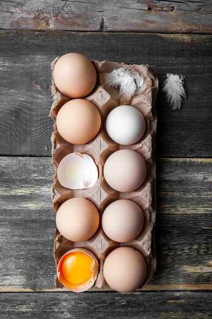 Eggs with cracked ones top view on a dark wooden background, vertical