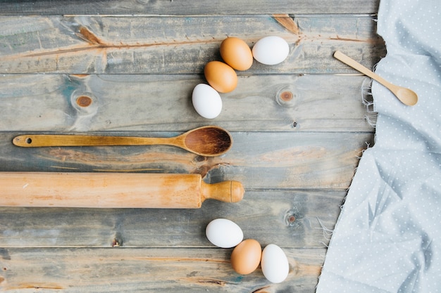 Eggs with rolling pin and spoon on wooden background