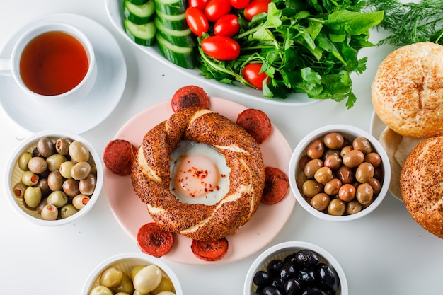 Uova con salsiccia in un piatto con una tazza di tè, bagel turco, vista dall'alto di insalata su una superficie bianca