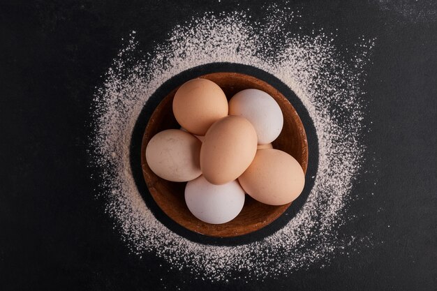 Eggs in a wooden cup on black surface, top view. 