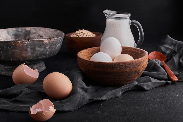 Free photo eggs in a wooden cup with a jar of milk on black backgorund.