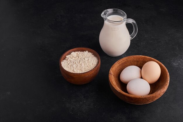 Яйца в деревянной чашке с молоком и мукой вокруг.