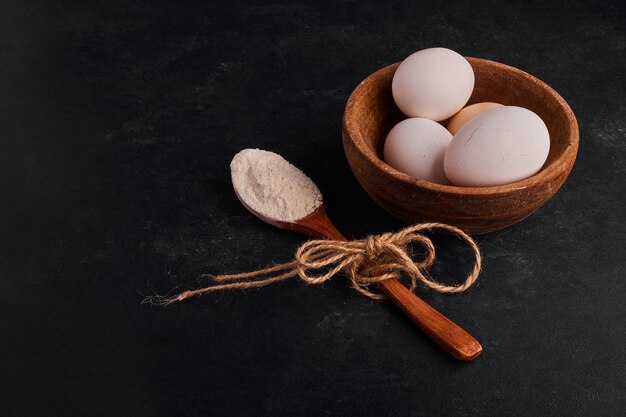 Eggs in a wooden cup with a spoon of flour. 