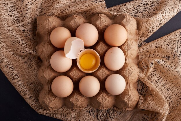 Eggs and yolk inside eggshell in the cardboard tray on a piece of burlap, top view. 