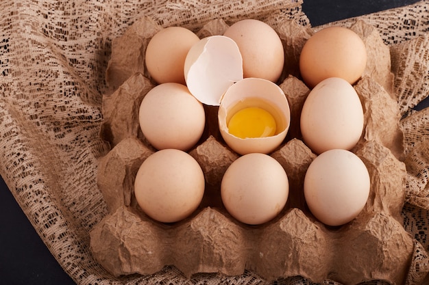 Яйца и желток в яичной скорлупе в картонном лотке на кусочке мешковины.