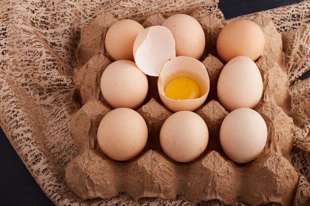 Eggs and yolk inside eggshell in the cardboard tray on a piece of burlap. 