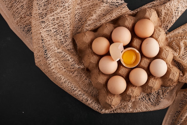 Яйца и желток в яичной скорлупе в картонном лотке на кусочке мешковины.