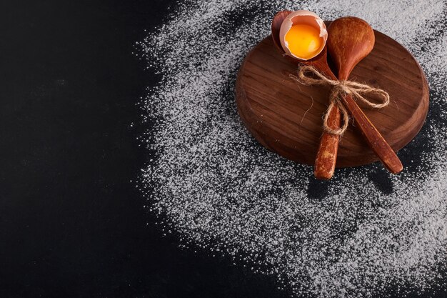 Eggshell with yolk in a wooden spoon on wooden platter. 