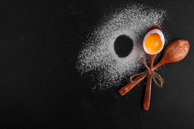 Eggshell in a wooden spoon on flour surface, top view. 