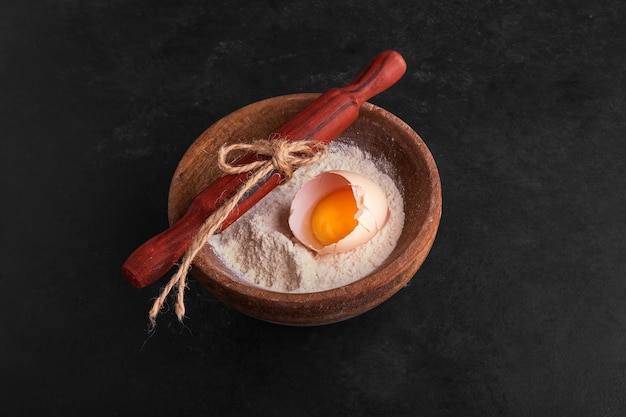 Free photo eggshell and yolk inside a flour cup on black surface.