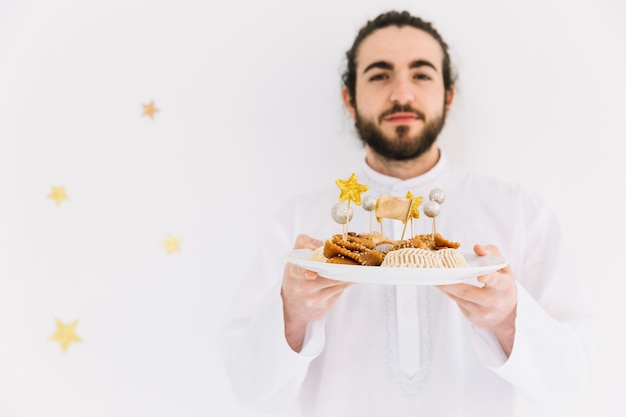 Free photo eid al-fitr concept with man presenting arab pastry