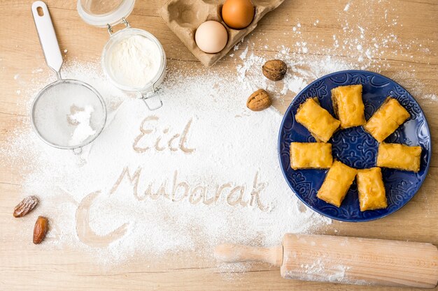 Eid Mubarak inscription on flour with eastern sweets on plate 