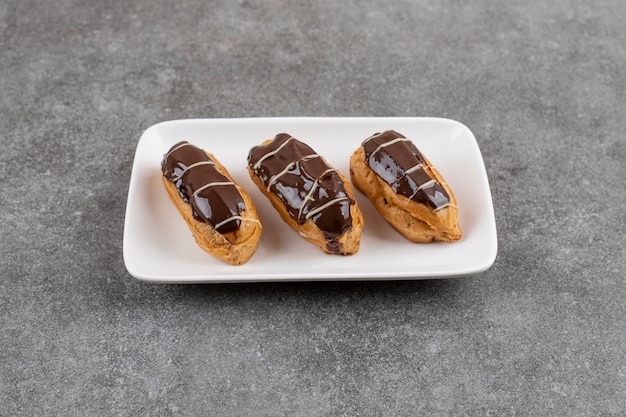 Бесплатное фото Пончик шоколада макаронных изделий ekler на белой плите над серой поверхностью взгляд сверху. самодельный.