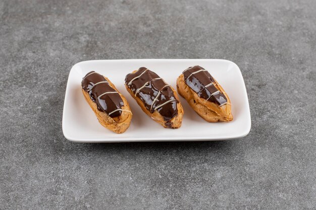 Ekler pasta chocolate donut on white plate over grey surface. Homemade . 