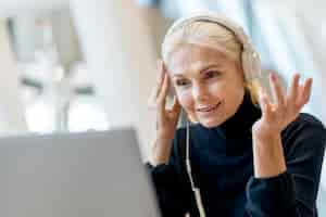 Free photo elder business woman having a video call on laptop with headphones