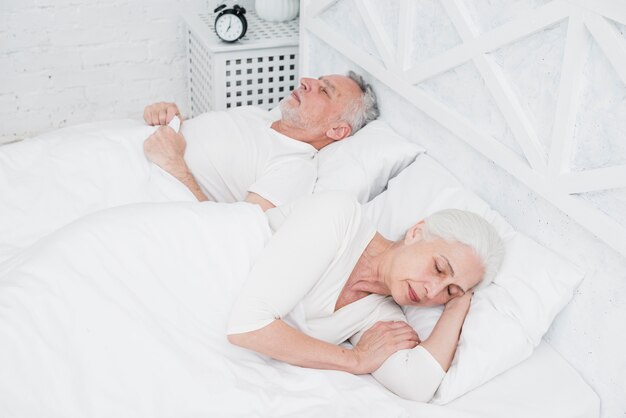 白いベッドで寝ている年配のカップル