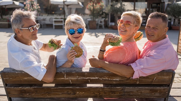 Бесплатное фото Пожилые пары на пляже вместе едят гамбургеры