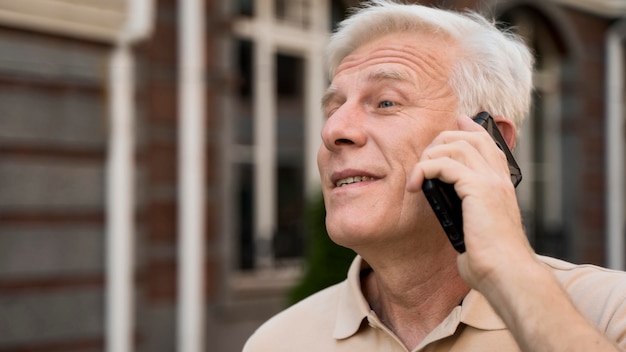 Free photo elder man taking on smartphone while out in the city