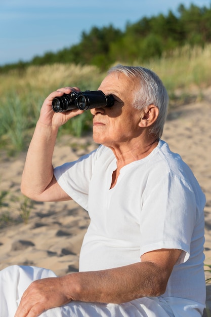 Пожилой мужчина с помощью бинокля на пляже, чтобы исследовать природу