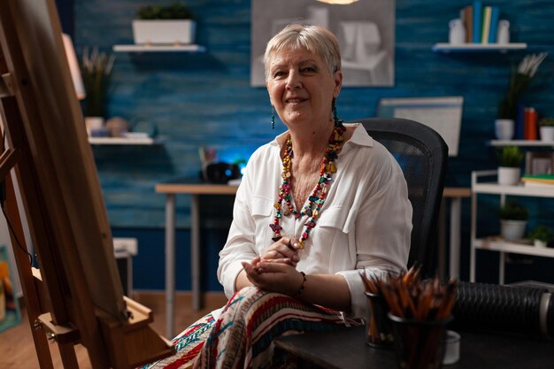 Elder person prepared to draw on canvas for art project while sitting in workshop space. Senior artist thinking about masterpiece and inspiration for drawing at studio. Woman with artistic vision