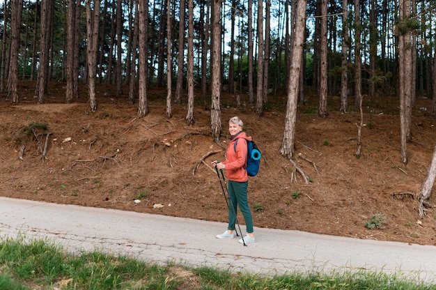 Donna anziana turistica con bastoncini da trekking nella foresta