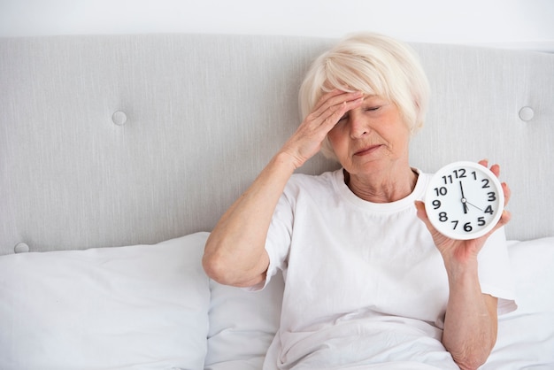 Elder woman holding a clock in her bed