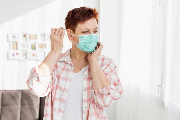 Elder woman putting on medical mask at home