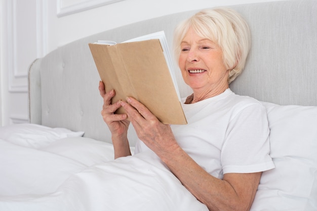 Пожилая женщина читает книгу в спальне