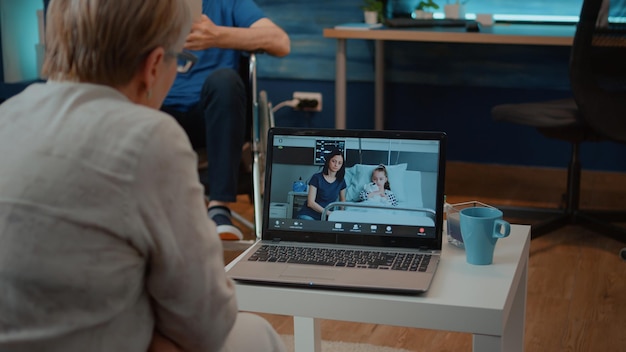 Elder woman using conference call on laptop for remote communication with daughter and girl in hospital. Old adult talking to family on online videoconference for telecommunication.