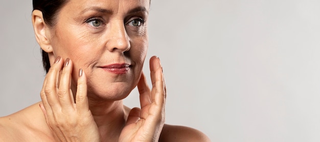 Elder woman with make-up on posing with hands on face and copy space