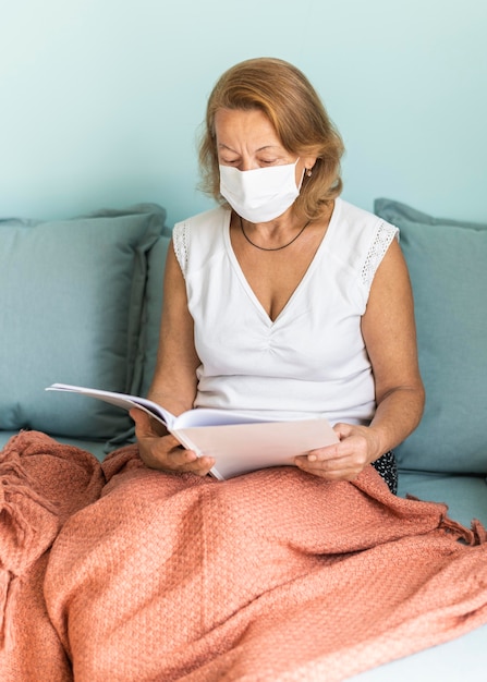 Foto gratuita donna anziana con mascherina medica a casa durante la pandemia leggendo un libro