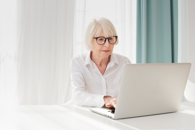 그녀의 사무실에서 노트북에서 일하는 노인 여성