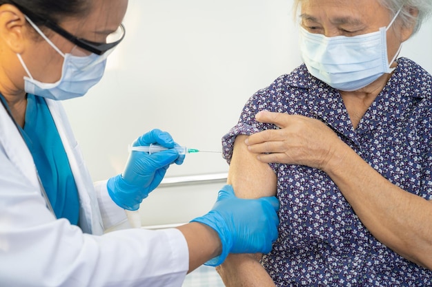 フェイス​マスク​を​着用している​高齢​の​アジア人​の​年配​の​女性​が​、​医師​によって​covid​-​19​または​コロナウイルスワクチン​を​接種しています​。
