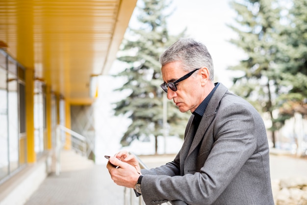 Foto gratuita uomo d'affari anziano che utilizza telefono cellulare all'aperto