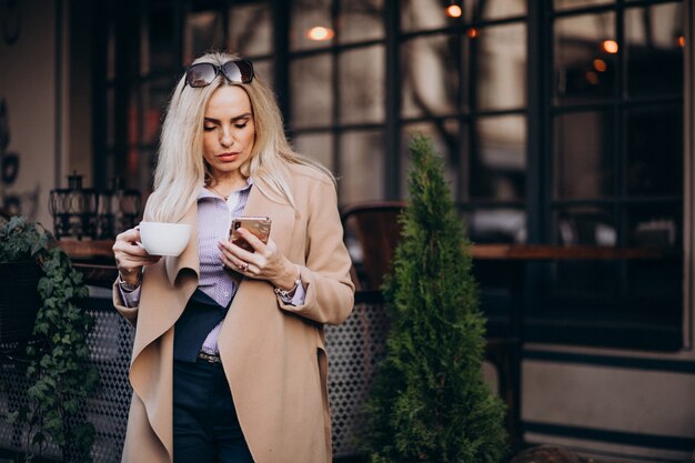 Elderly businesswoman drinking coffee outside cafe and talking on the phone