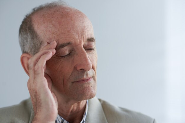 Elderly Caucasian businessman massaging temple with closed eyes