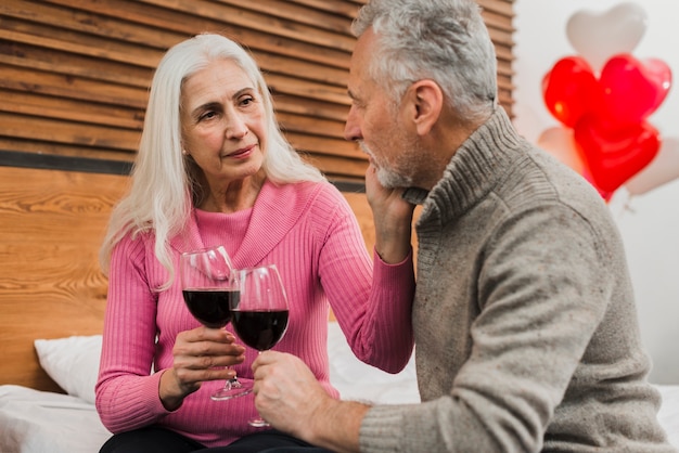 Free photo elderly couple on bed drinking wine