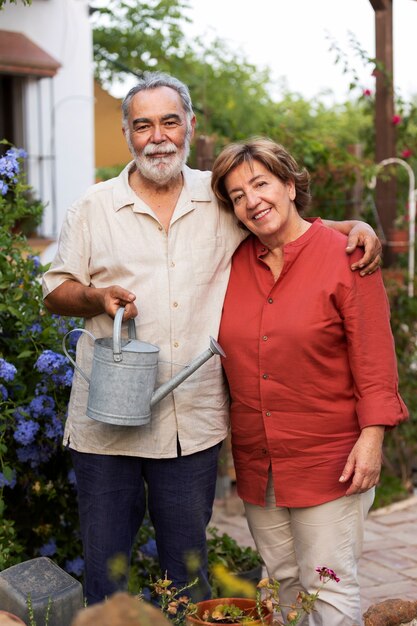 Elderly couple holding watering can while embracing each other in their countryside home