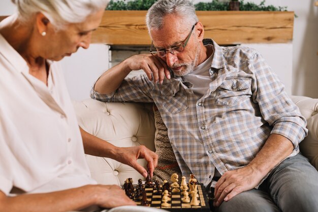 An elderly couple sitting on sofa playing chess