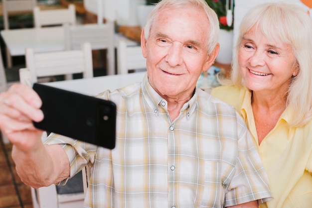 Пожилая пара принимает селфи, улыбаясь дома