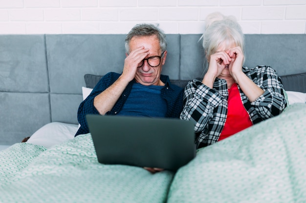 Elderly couple with headache in bed with laptop