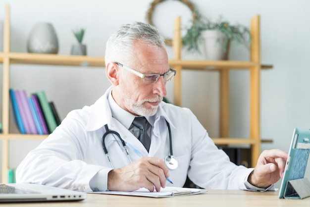Elderly doctor using tablet and making notes