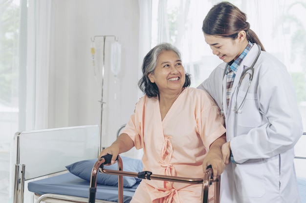 Elderly female smiling with young female doctor visiting senior patient woman at hospital ward