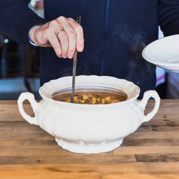 Foto gratuita mani anziane mettendo gustosa zuppa sul piatto in cucina