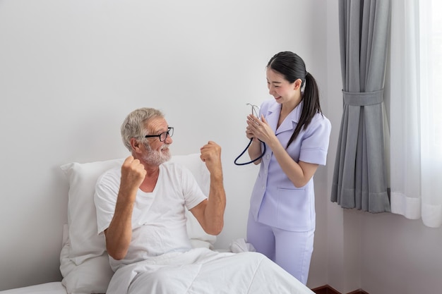 Elderly man healthy rise fist up with happy nurse in bedroom at nursing home thumb up