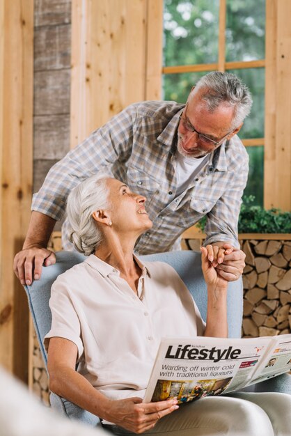 An elderly man holding hand of her wife sitting on chair with newspaper