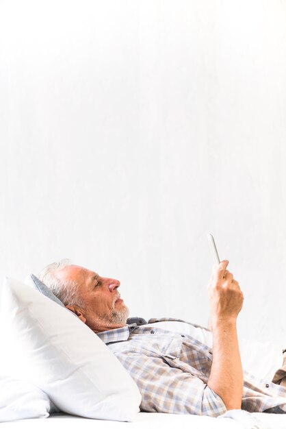 Elderly man lying on the bed looking at digital tablet